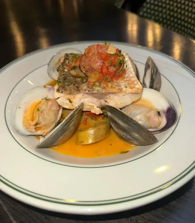 Fish fillet with clams and orange sauce on a white plate.