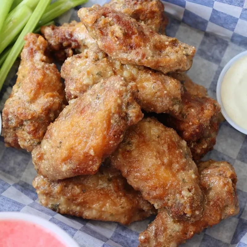 A basket of fried chicken wings with celery and two dipping sauces.