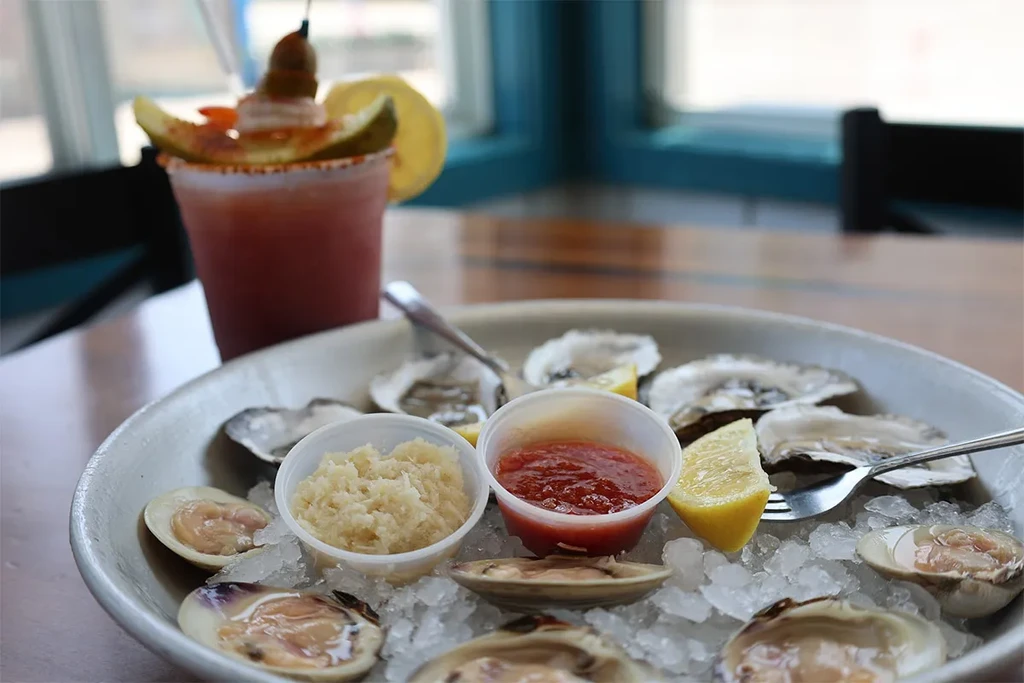 A Bloody Mary and a plate of raw oysters and clams on ice.