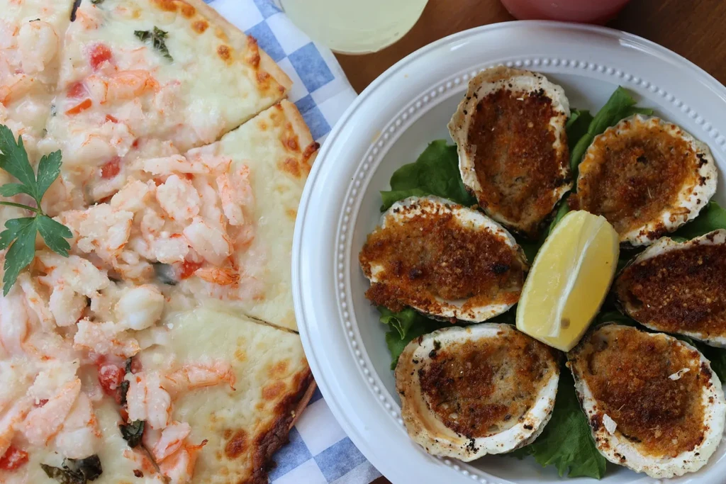 Shrimp pizza and a plate of baked oysters with a lemon wedge.