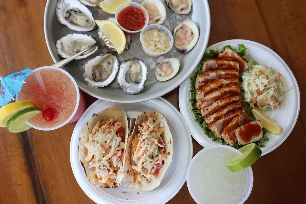 A table full of seafood dishes, including oysters, fish tacos, and seared tuna.
