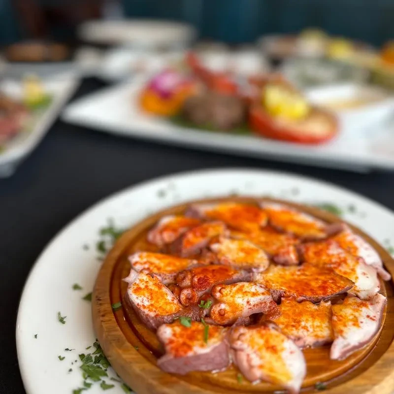 Sliced octopus with paprika on a wooden plate, parsley garnish.