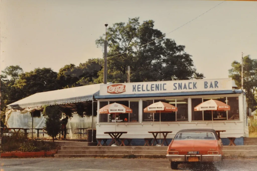 Exterior view of Hellenic Snack Bar with an orange car parked outside.