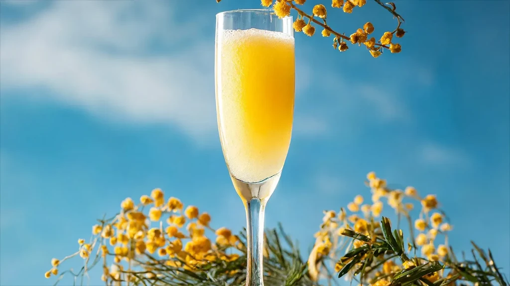 A flute glass of orange juice and champagne with yellow flowers.