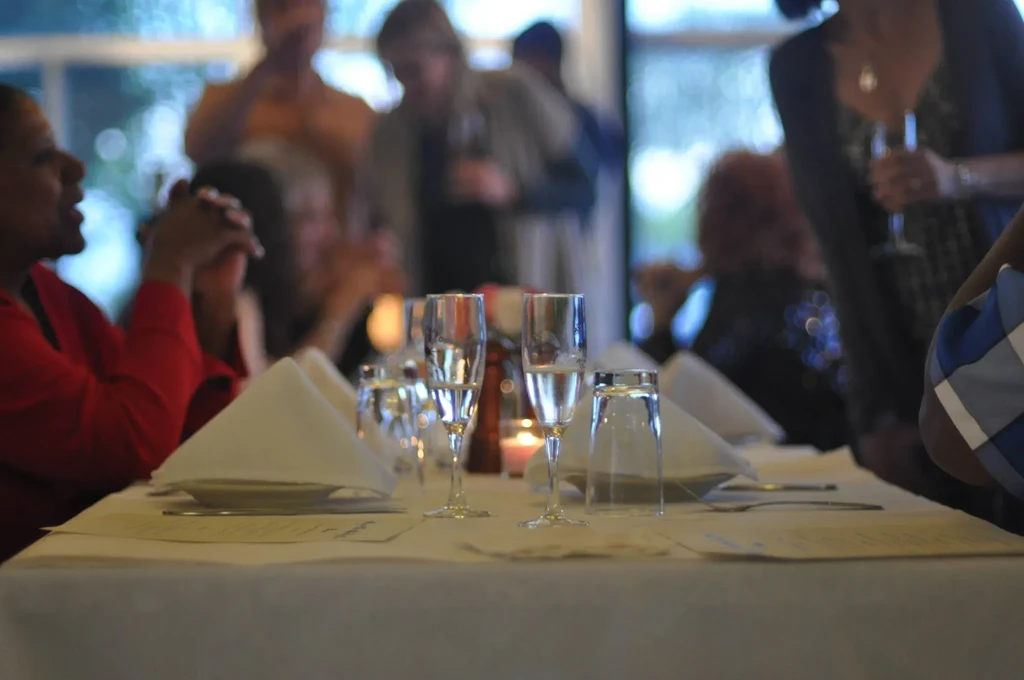 Dining table set with glasses and people socializing in the background.