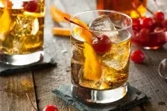 Two Old Fashioned cocktails with orange peel and cherry garnishes.