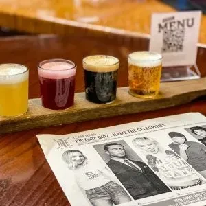 Beer flight and celebrity picture quiz on a wooden pub table.