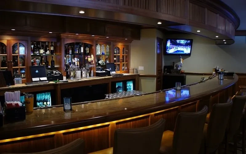 Empty, dimly lit bar with a curved wooden counter and liquor bottles.