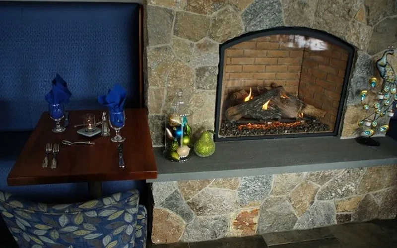 Set restaurant dining table by a rustic stone fireplace with flames.