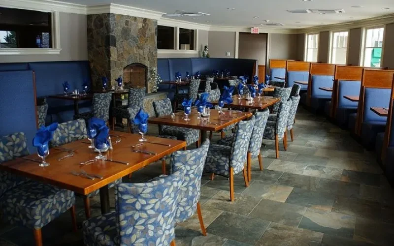 Empty restaurant dining room with blue napkins and a stone fireplace.