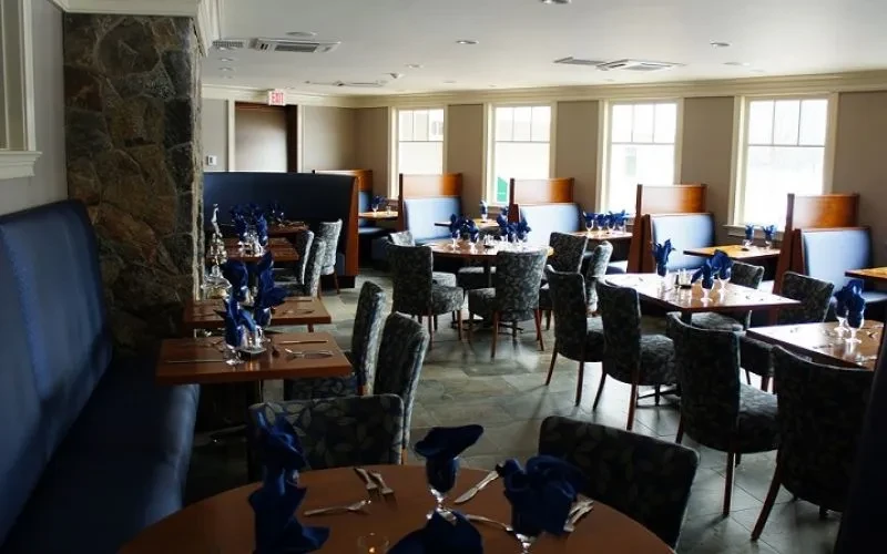Well-lit dining room with blue booths, set tables, and stone pillar.
