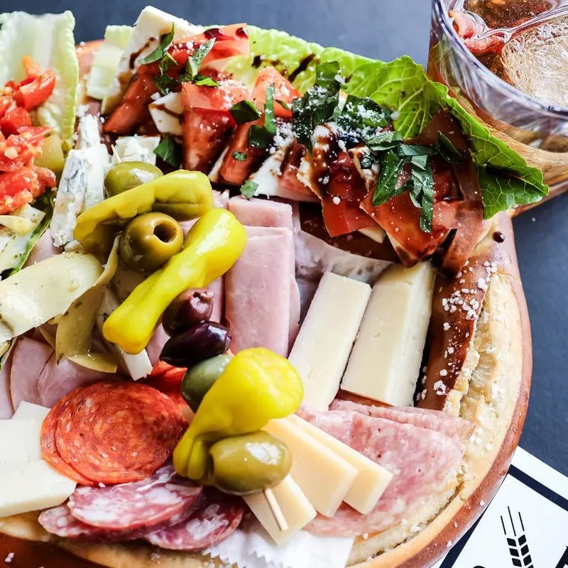 A rustic charcuterie board with meats, cheeses, olives, tomatoes, and pretzel bread.