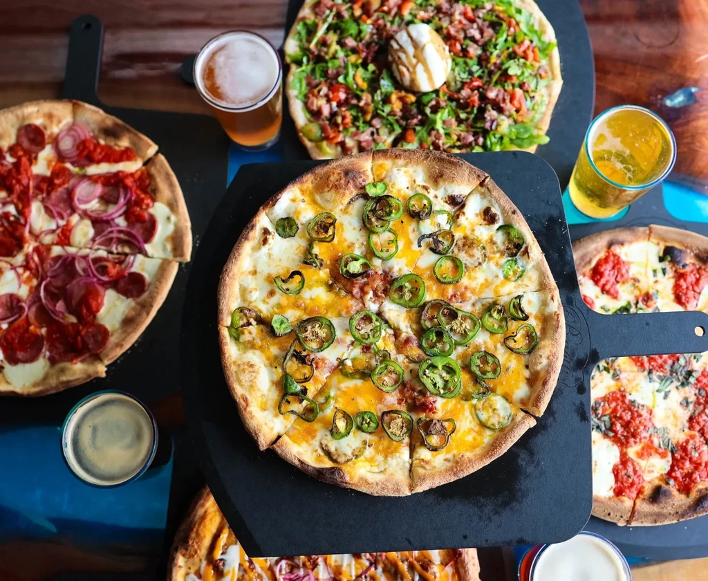 An overhead shot of several pizzas and beers on a table.