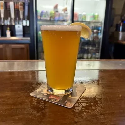 Golden beer with foam and lemon wedge on a bar top.