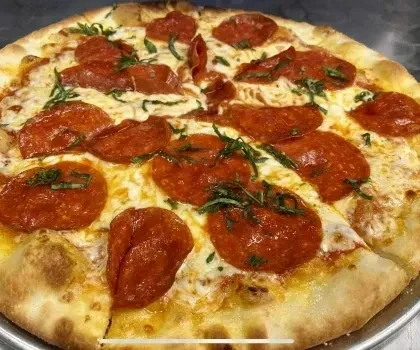 Freshly baked pepperoni pizza with melted cheese and green herbs.