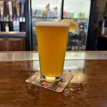 Pint glass of golden beer with lime slice on a bar.