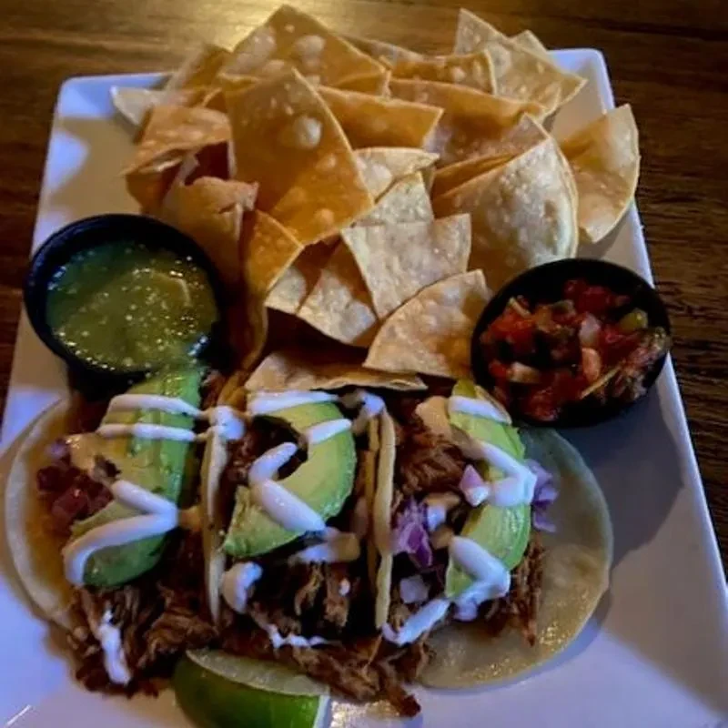 Plate with three shredded meat tacos, chips, green and red salsas.