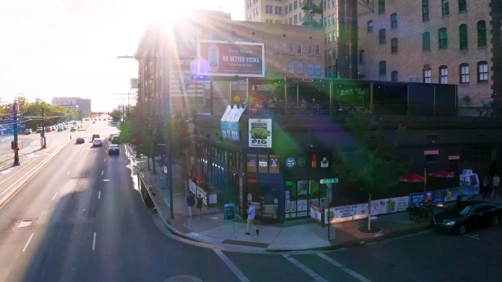Elevated urban corner with sun flare, street bar, and rooftop patio.