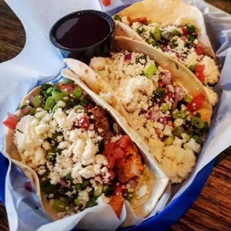 Three loaded tacos with meat, cheese, onions, tomato, and sauce.