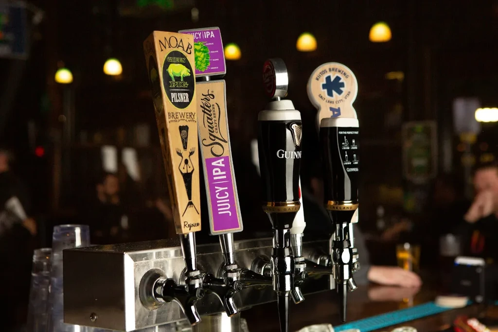 Close-up of multiple branded beer taps on a dimly lit bar.