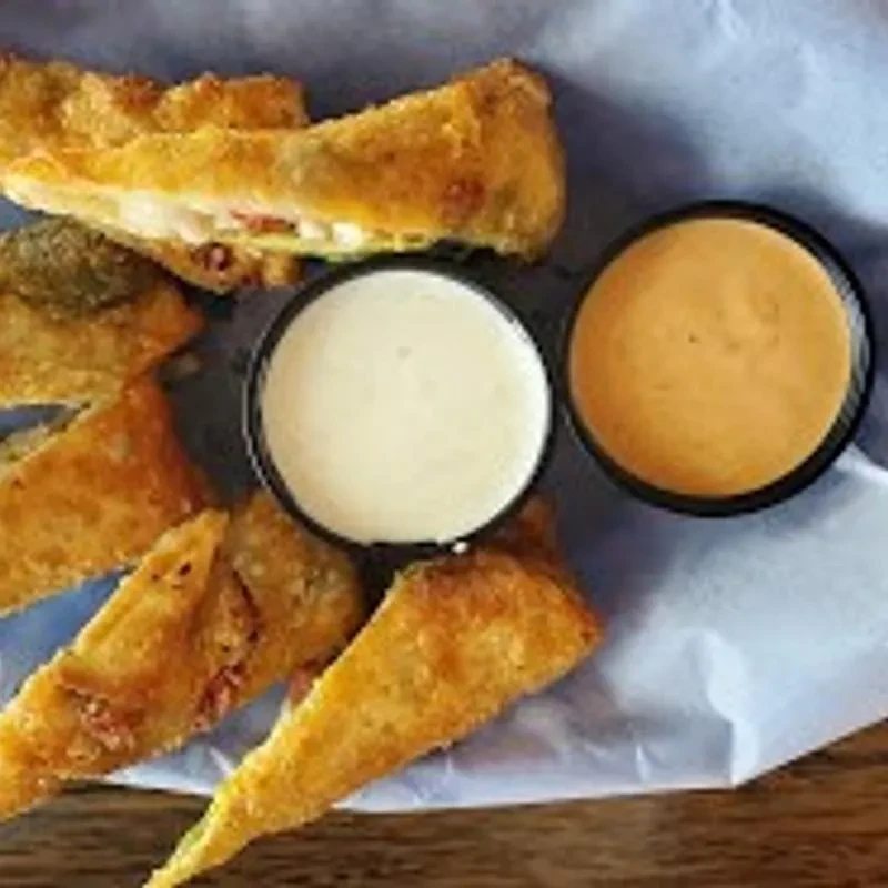 Fried cheesy appetizers with two dipping sauces on a wooden surface.