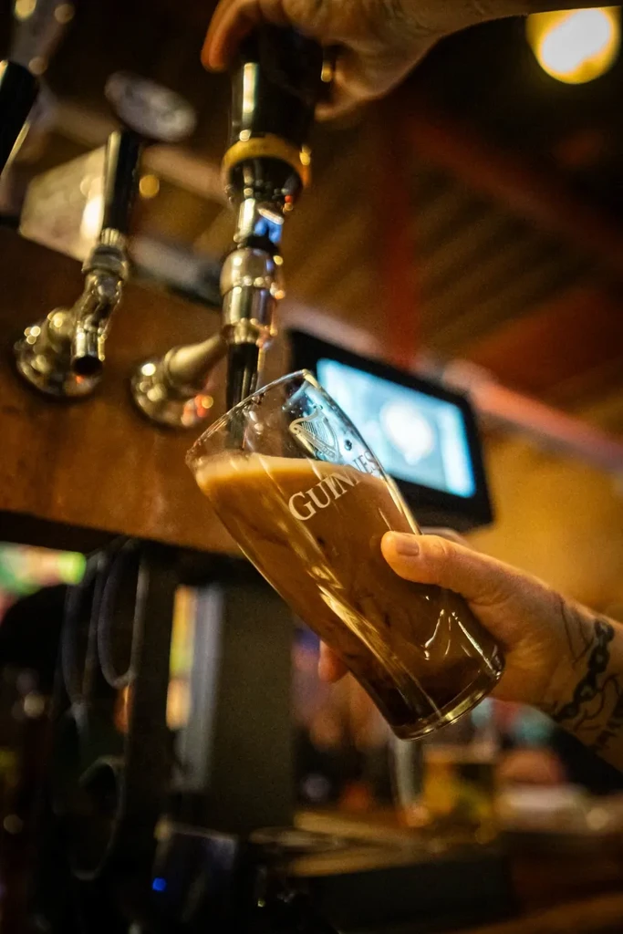Guinness beer pouring into a branded glass held by a tattooed hand.