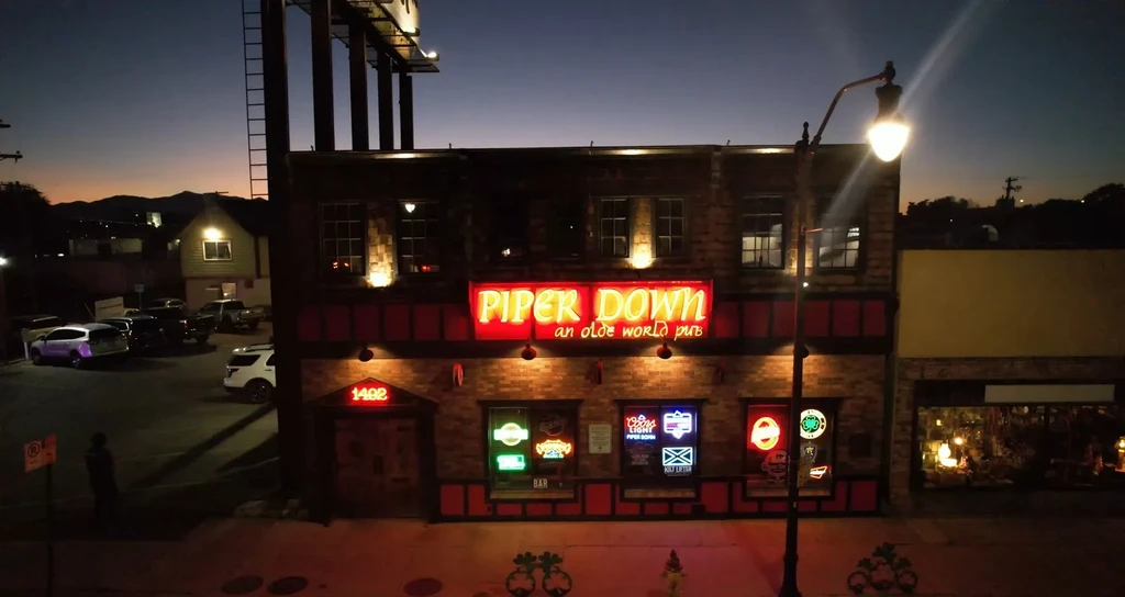 Exterior of Piper Down pub with vibrant neon lights at dusk.