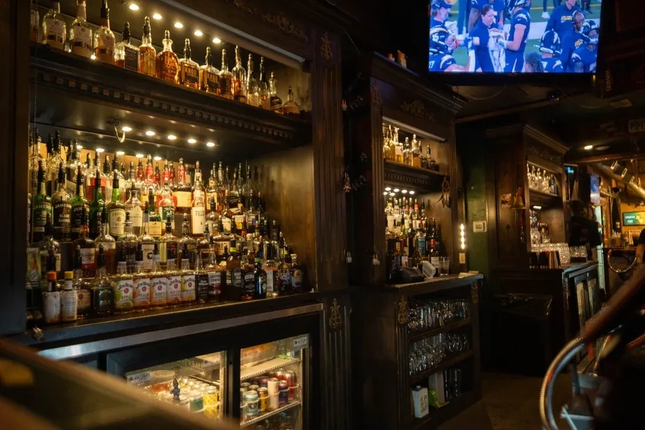 Dimly lit bar with extensive liquor bottle collection and sports on TV.