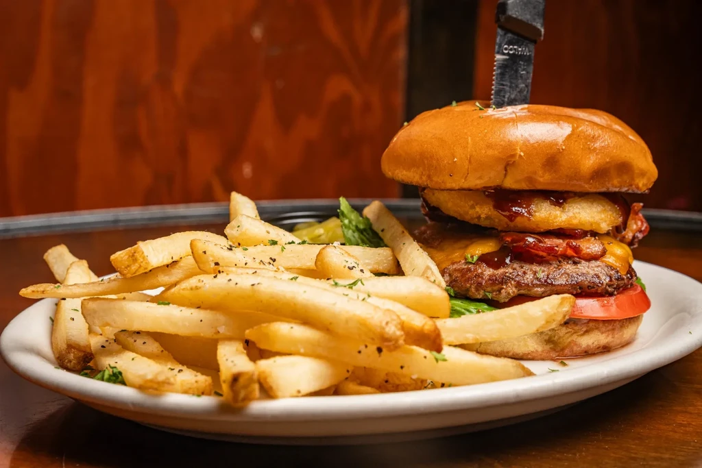 Loaded gourmet burger with fries and knife on a white plate.