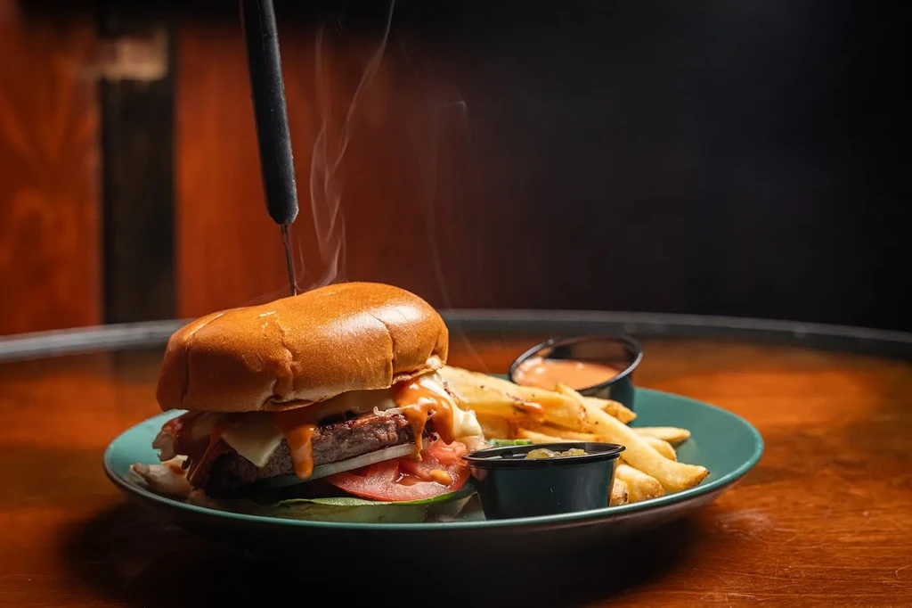 Hot gourmet burger and golden fries with sauces on a teal plate.