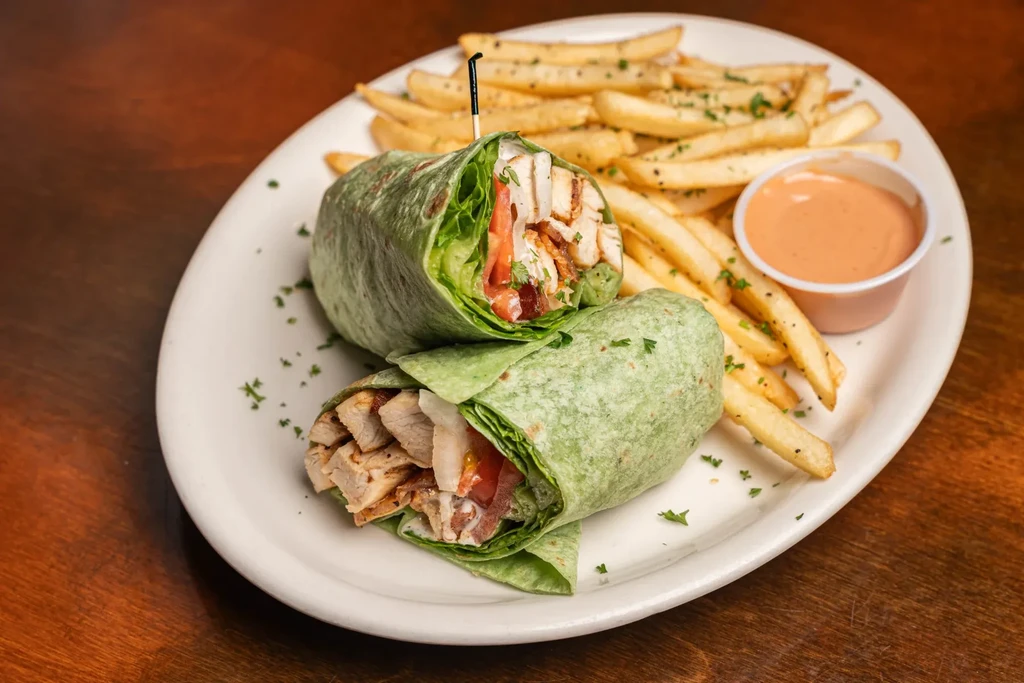 Plate of green chicken wraps, french fries, and orange dipping sauce.