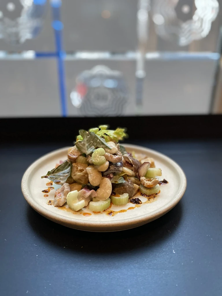 Close-up of hearty, stew-like dish with octopus, beans, celery, cashews.
