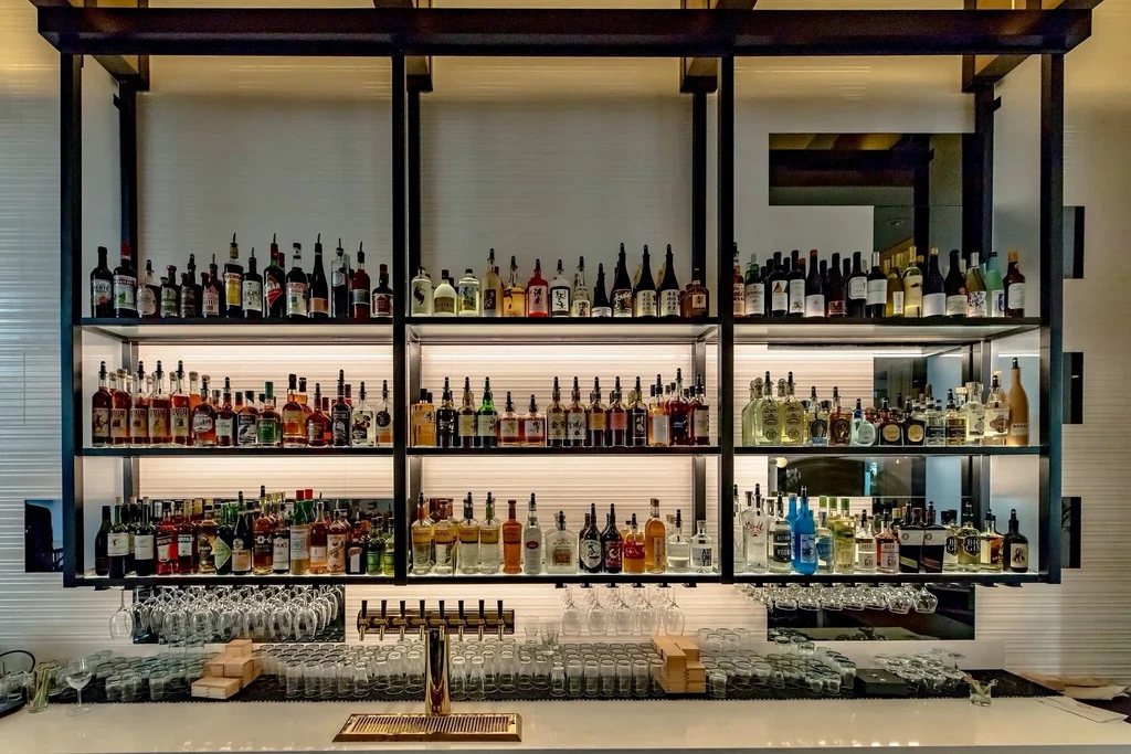 Modern bar with illuminated shelves of bottles, glassware, and brass taps.