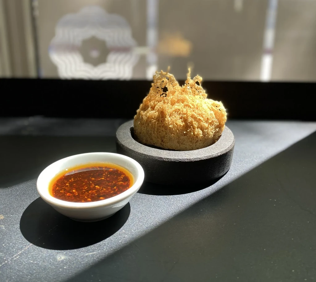 Intricately fried golden food with dipping sauce on a dark surface.
