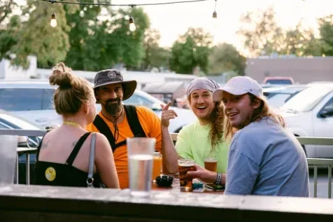 Four people converse and drink at an outdoor evening patio.