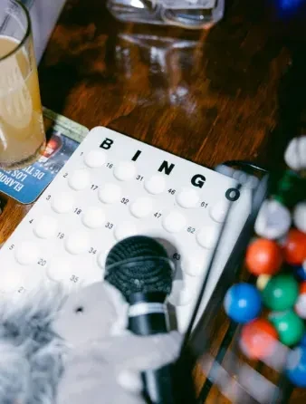 Bingo card, drink, microphone, and bingo balls on a wooden table.