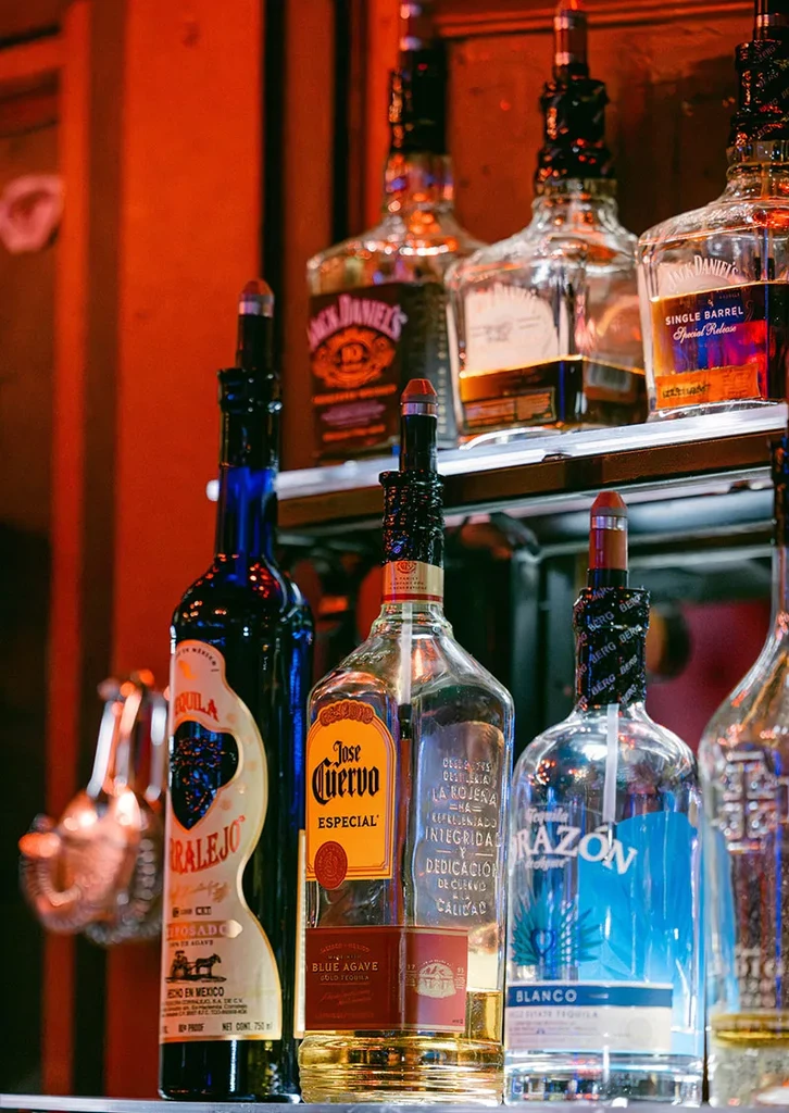 Assorted tequila and whiskey bottles displayed on warmly lit bar shelves.