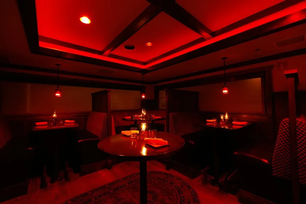Red-lit restaurant dining room with set tables and booths.