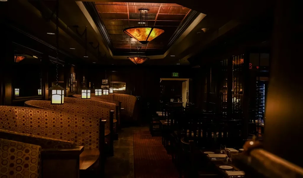 Empty restaurant interior with curved booths, amber lights, and set tables.