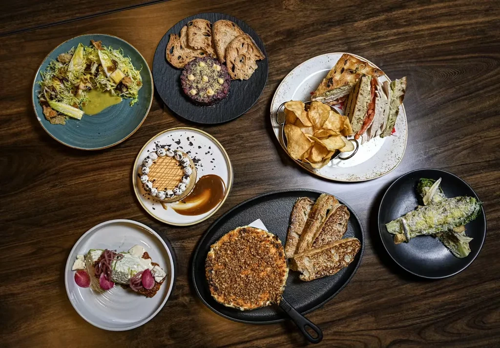 Overhead shot of seven diverse dishes artfully arranged on a dark wooden table.
