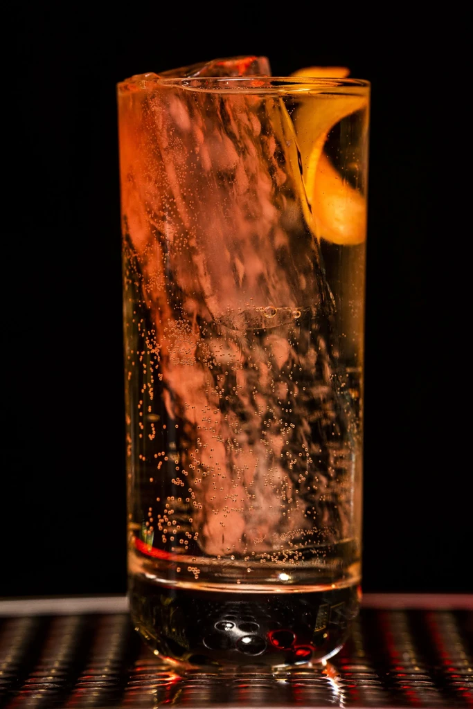 Amber carbonated drink with ice and orange peel, dramatically lit.