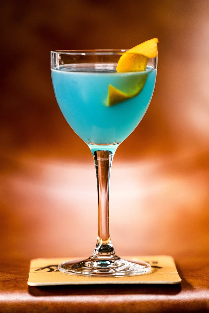 Vibrant blue cocktail in coupette glass with citrus peel garnish.