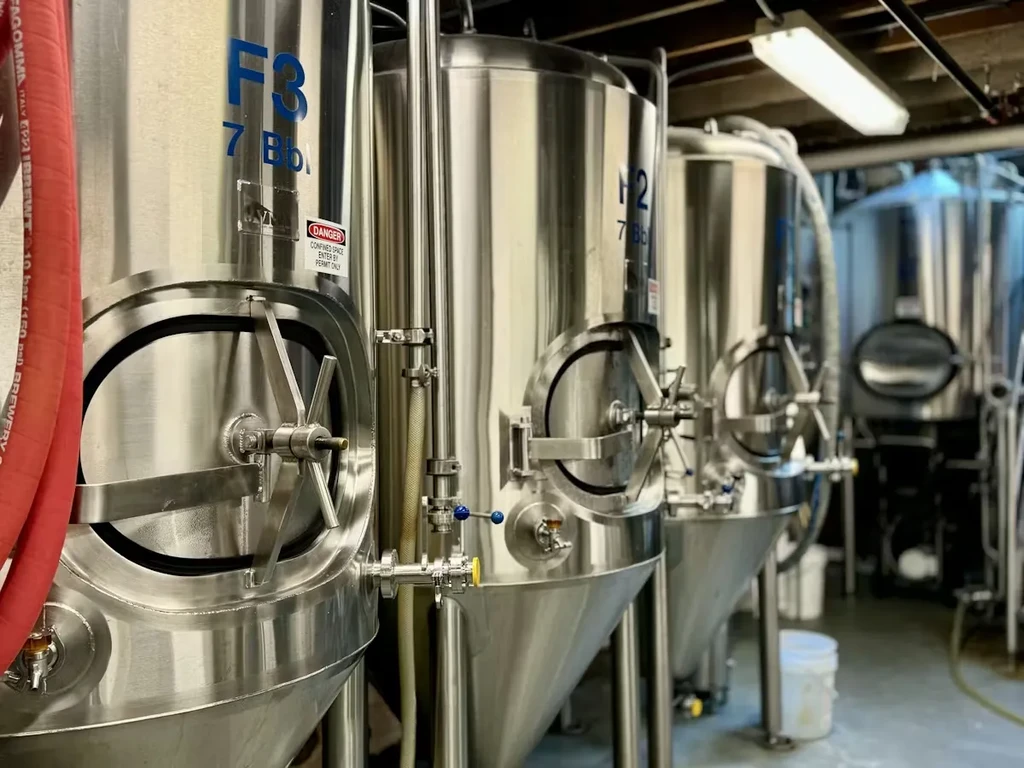 Gleaming stainless steel conical fermentation tanks in a clean industrial brewery.