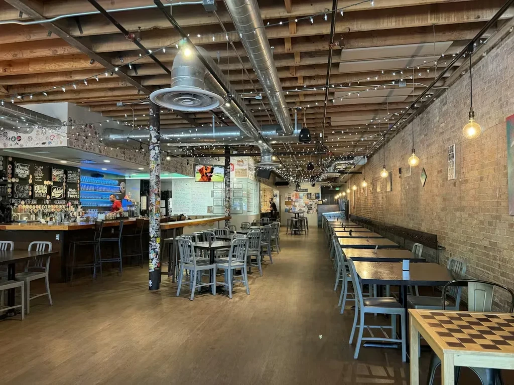 Restaurant interior featuring a long bar, exposed ceiling, and warm lights.