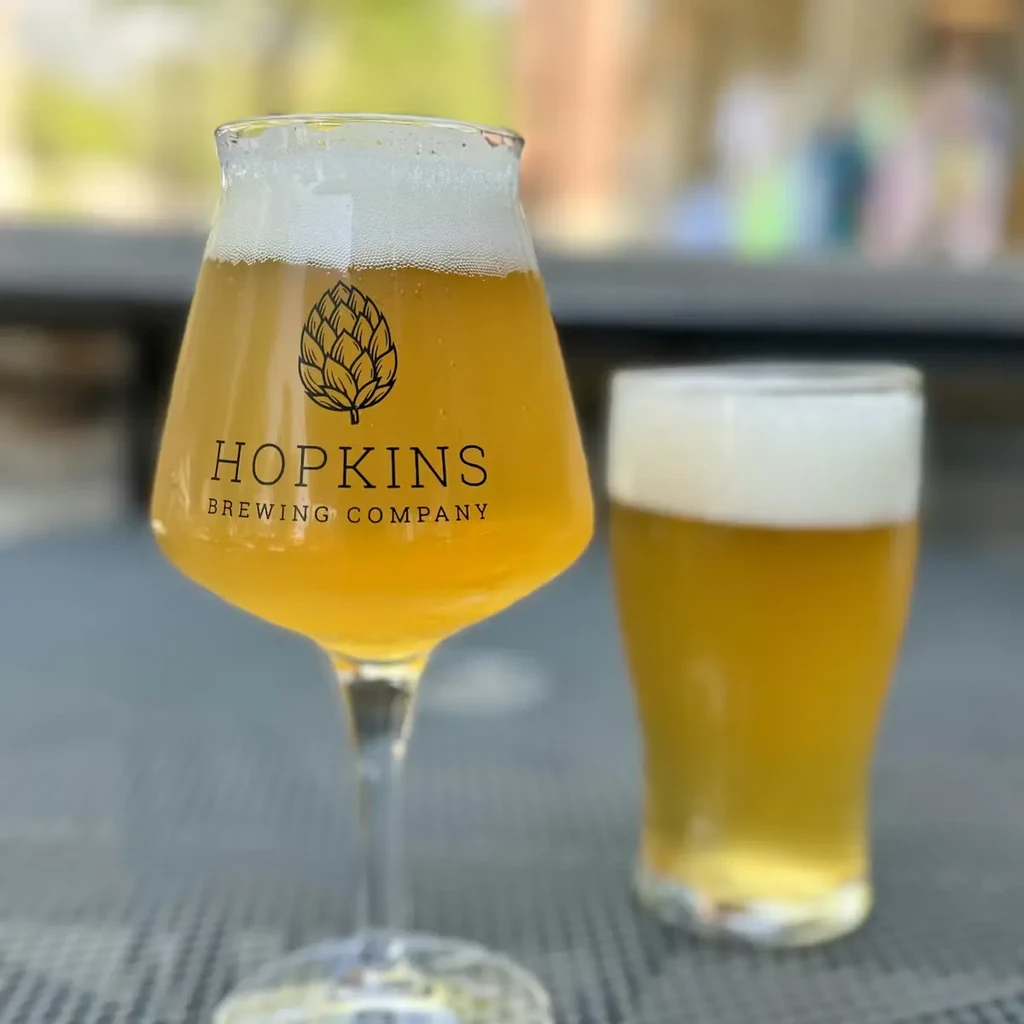 Hopkins Brewing Company beer glass and blurred pint on an outdoor patio.