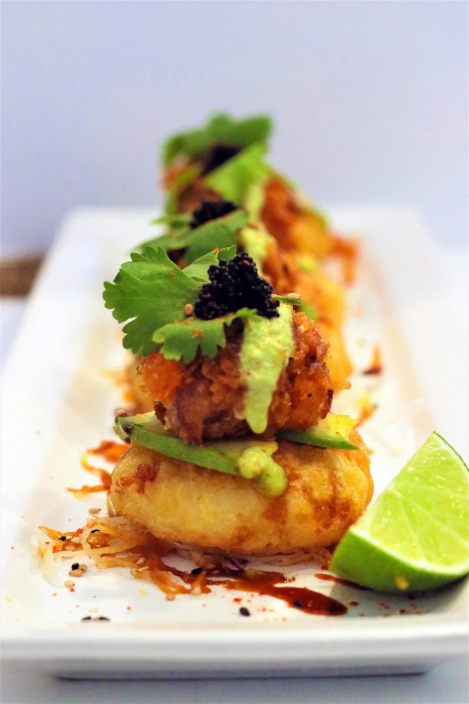 Four appetizers with golden bases, avocado, crispy balls, caviar, and lime.