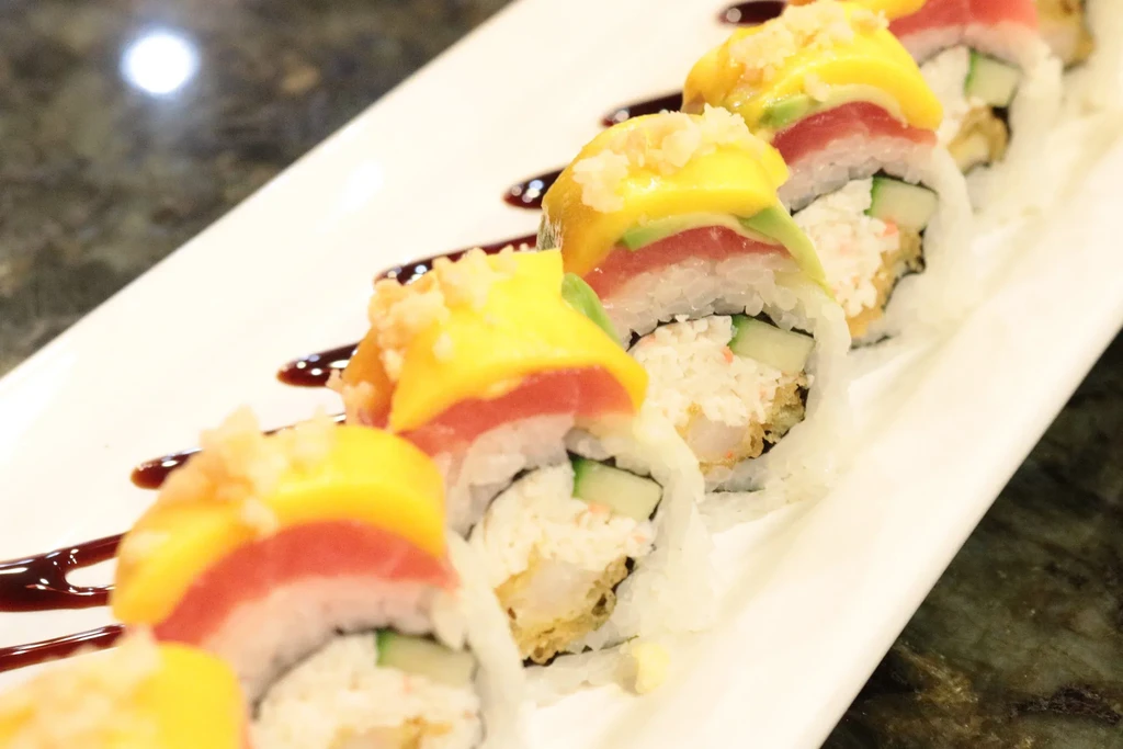 Eight colorful sushi rolls topped with mango, tuna, and avocado.