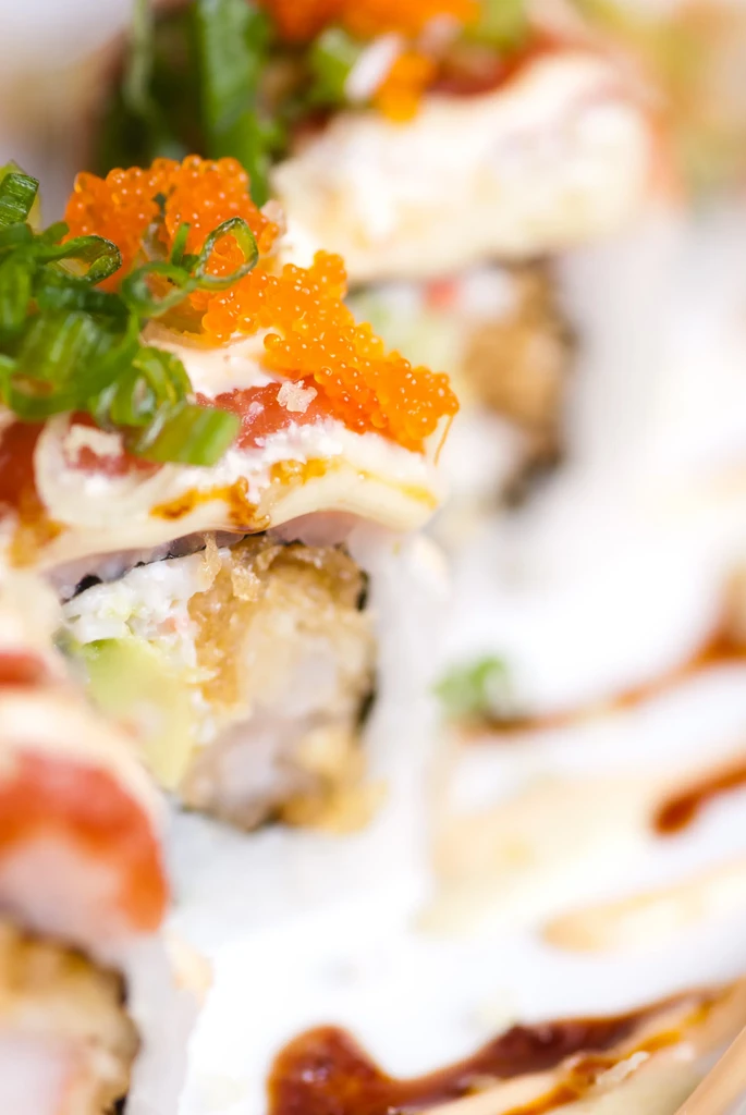 Close-up of sushi rolls with tobiko, green onions, white, and dark sauces.