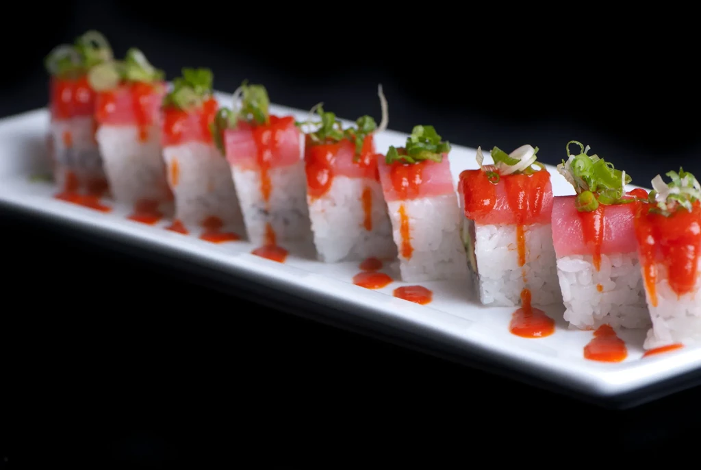 Eight sushi pieces with red sauce, green onions, white plate, black background.