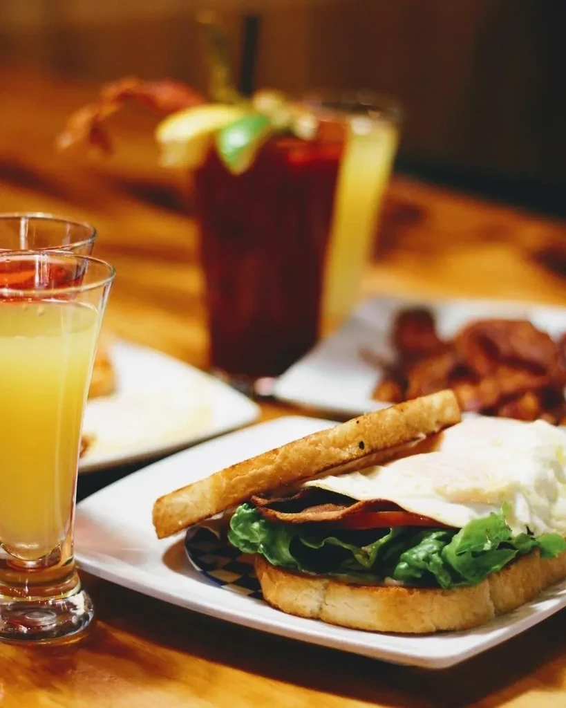 Close-up of an open-faced breakfast sandwich, orange juice, and Bloody Mary.
